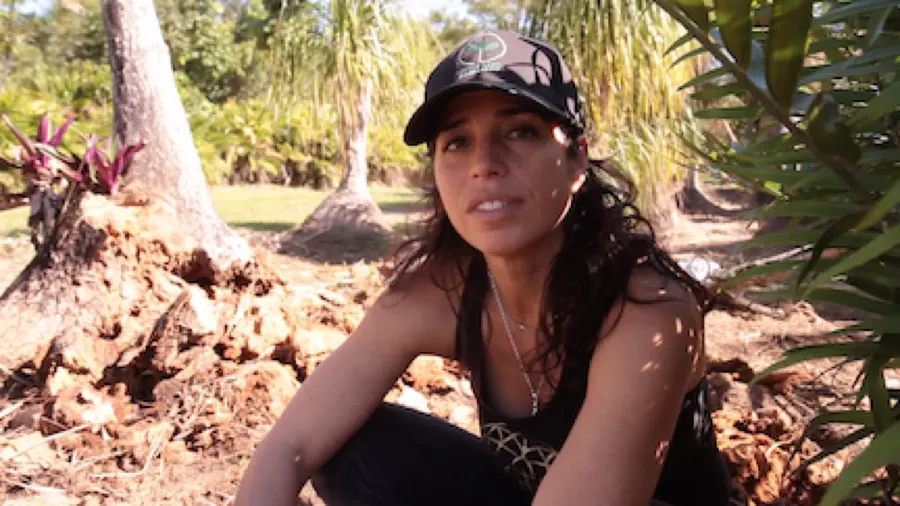 Dr. Lanette Sobel kneeling in rich soil among palms at the Fertile Earth farm