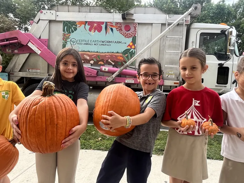 Elementary students holding large pumpkins in front of the Fertile Earth collection truck