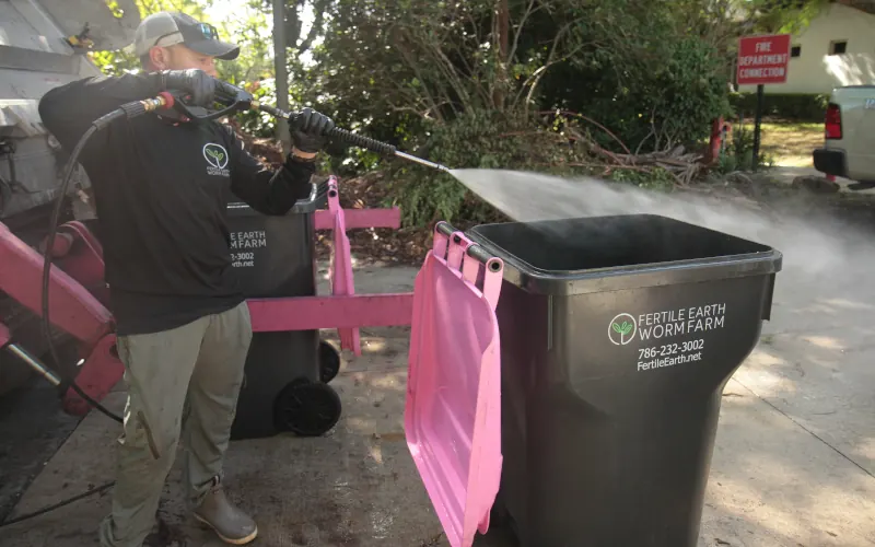 A Fertile Earth driver pressure-washing a toter at pickup