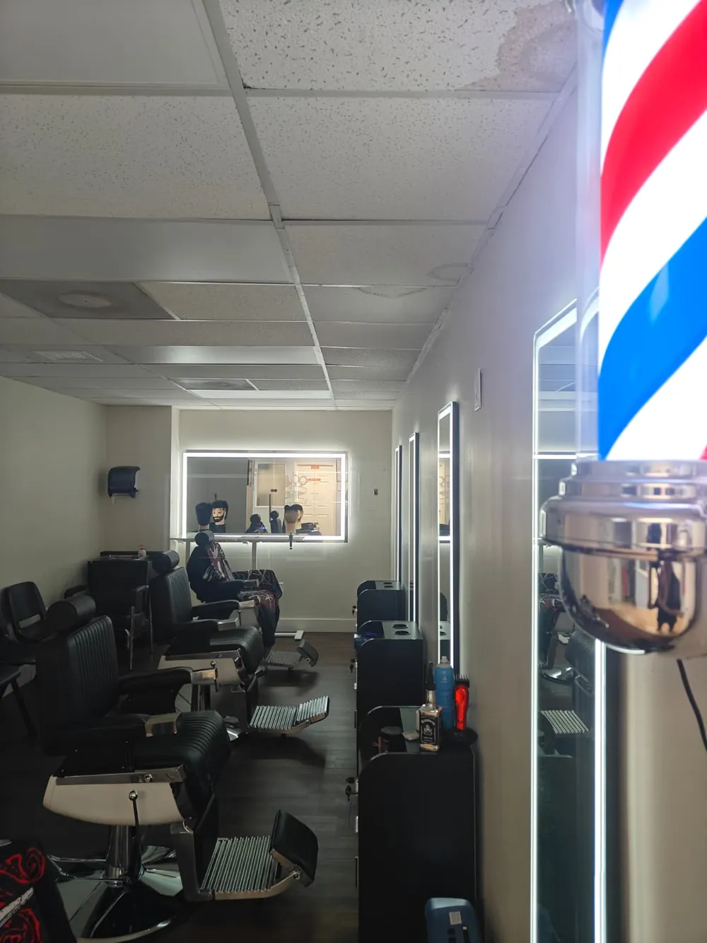 Barbering lab at Florida Professional Institute with a barber pole, black barber chairs and lit mirrors
